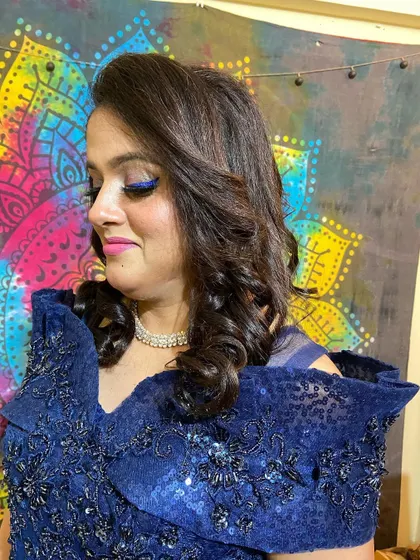 A bold party makeup look with a vibrant blue winged eyeliner and soft curls.
