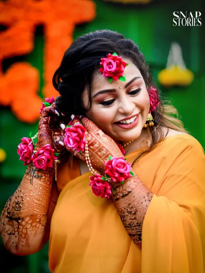 A close-up of the bride, smiling as she adjusts her floral jewelry. We capture the intricate details of your Haldi look, from the floral accessories to the henna.