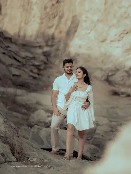 A romantic pre-wedding portrait in a rocky, natural landscape. The couple's casual white outfits create a soft and beautiful contrast with the surroundings.