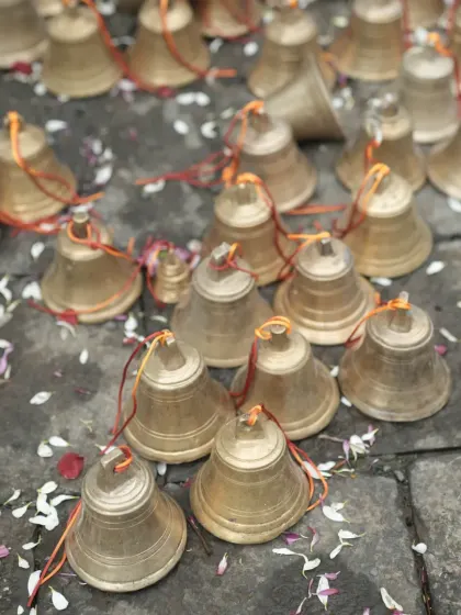 A collection of small brass bells laid out on the stone floor, waiting to be used in the decor, scattered with flower petals.