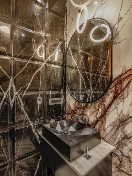 I believe every corner of a home deserves personality. In this powder room, I used bold, dark marble with intricate veining and beveled wall tiles to create a sense of depth. A custom geometric basin and modern ring lighting complete this statement of compact luxury.