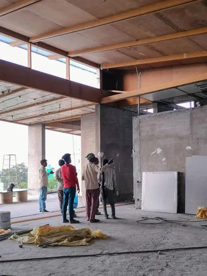 Inside House K, workers stand within the large, open-plan space. The image shows the exposed steel beams and wooden underlay of the roof structure.