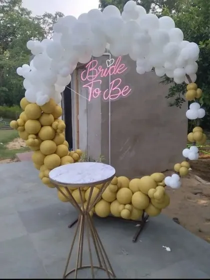 This unique moon-shaped balloon arch is perfect for an outdoor or terrace party. The design uses mustard yellow and white balloons to form a crescent moon, with a 'Bride To Be' neon sign glowing in the center.