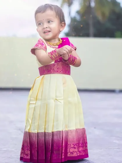A full-length view of the cream and pink Pattu Pavadai. The pleated skirt allows for easy movement, and the silk fabric with its wide zari border gives it a classic, festive look.