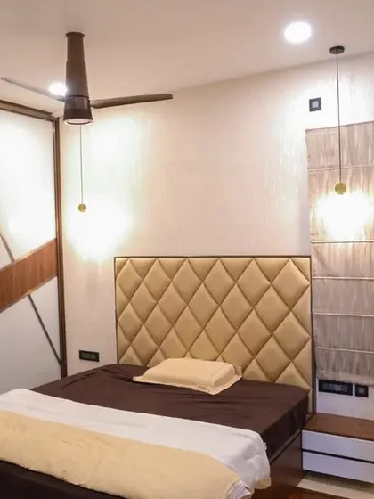 The master bedroom in the Velachery apartment, designed for comfort with a diamond-patterned cushioned headboard and a stylish sliding wardrobe with a geometric wood and white finish.