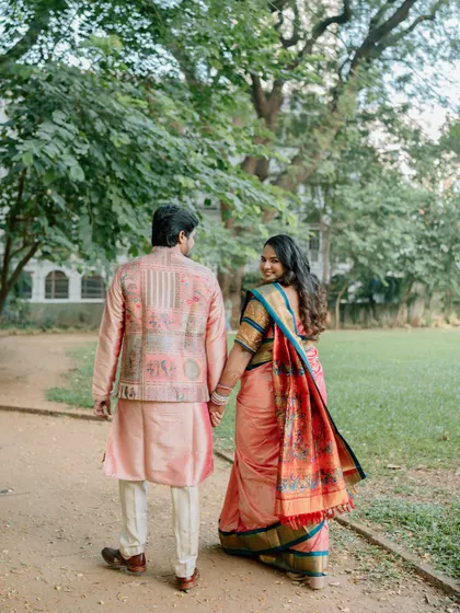 A couple in traditional Indian wedding attire walks hand-in-hand through a park, with the bride looking back at the camera with a smile. This classic shot tells a story of starting a new journey together.