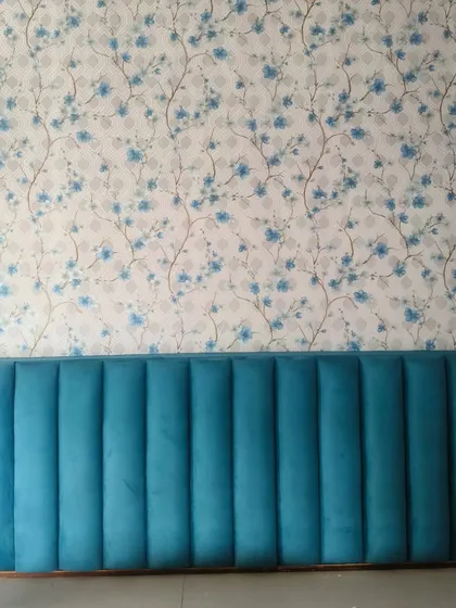 A beautiful floral wallpaper used as an accent behind a vibrant blue headboard. The soft blue flowers on the wallpaper complement the headboard perfectly, creating a cohesive and stylish look.