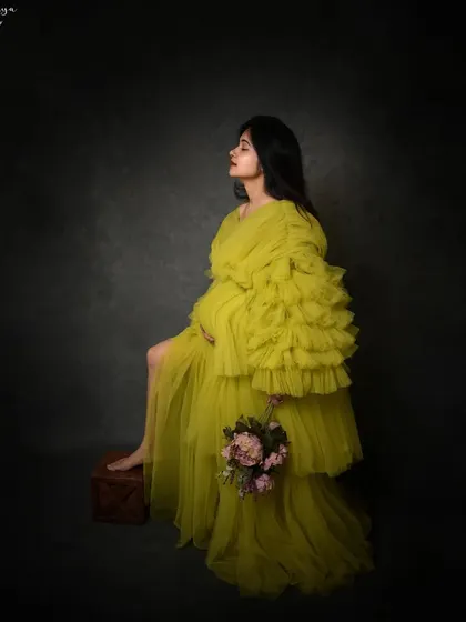 A full-body profile shot that showcases the dramatic silhouette of this tiered tulle gown, creating a high-fashion maternity look.