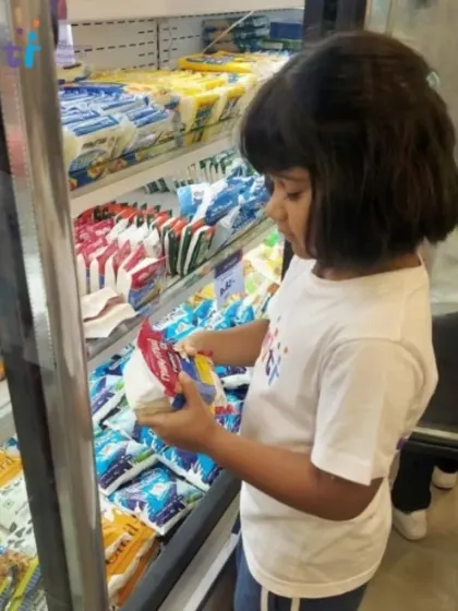 A child examines a packet of paneer in the refrigerated section, learning about different types of food and where they are stored in a supermarket.