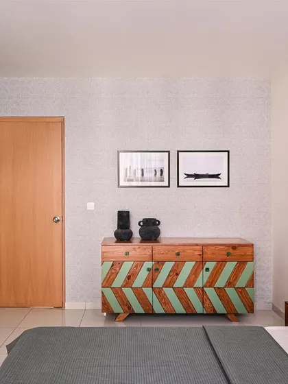 An earthy and cozy bedroom designed for the owner's father, featuring a sage green wardrobe and a custom-made chest of drawers with a chevron pattern.