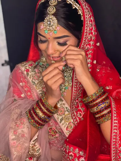 A candid moment of the bride adjusting her nose ring. The heavy bridal bangles and detailed dupatta border are beautifully featured.