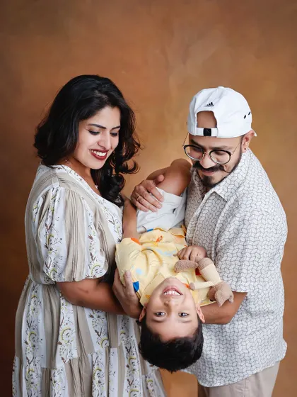 A fun and candid family portrait in the studio. The parents are holding their laughing child upside down, showcasing a playful and authentic moment that captures the family's dynamic.