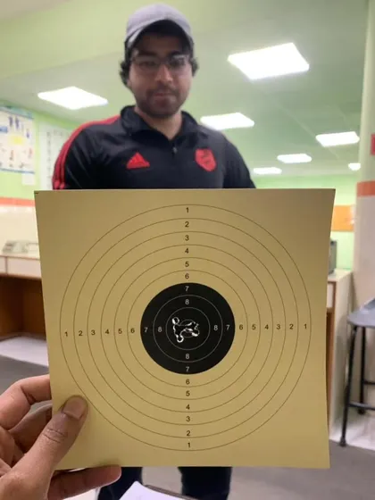 A student holding up his target, showing a very tight grouping of shots in the center. This is the result of consistent practice.