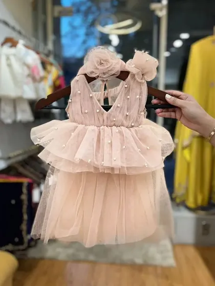 A product shot of our Ruffle Barbie dress. This piece features a pearl-studded bodice, layered tulle skirt, and floral shoulder details, ready to make any little girl feel special.