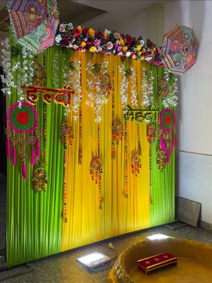 A side view of the Haldi-Mehendi decor, showing the depth and layers of the hanging decorations against the colorful draped background.