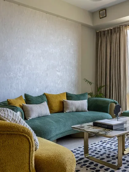 A full view of the living room's seating area, where neutral walls and curtains provide a calm backdrop for the colorful green and yellow sofas and patterned rug.