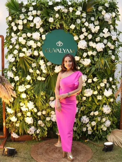 A guest poses in front of a lush floral wall we created for a corporate event. The wall is made of dense greenery and white flowers, with a custom brand logo.