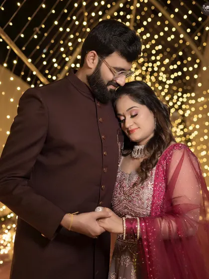 A romantic reception portrait of a couple against a backdrop of sparkling fairy lights. The groom gently holds the bride's hand as he rests his head on hers, creating a warm and intimate scene.