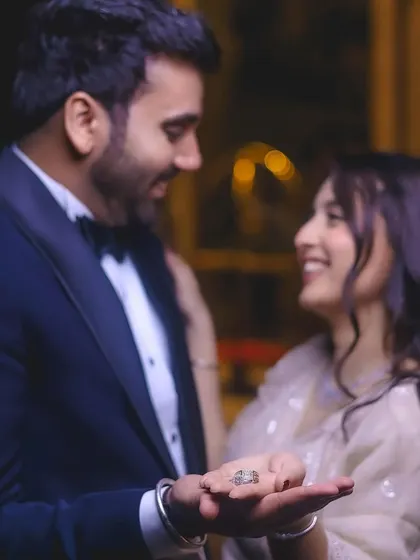 A creative engagement portrait focusing on the ring, held in the groom's hand, with the couple's happy faces in the background.