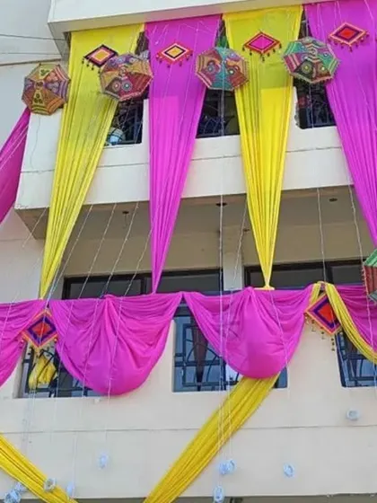 Balcony decoration featuring pink and yellow drapes accented with colorful hanging umbrellas and props.