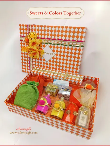 An open view of our orange checkered Holi box, revealing small bottles of colored water, sweet boxes, and other festive trinkets. It's a box full of surprises.