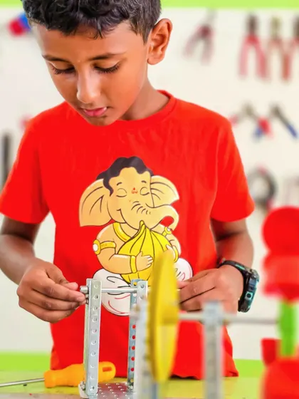 A close-up of a student assembling a complex mechanical model, carefully fitting together metal strips, gears, and screws.