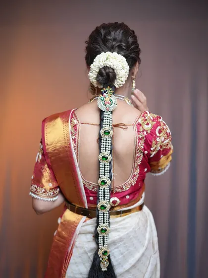 A traditional South Indian bridal braid, or jada, featuring jasmine flowers and stunning pearl and green stone jewelry. This is a classic hairstyle that I specialize in for wedding ceremonies.
