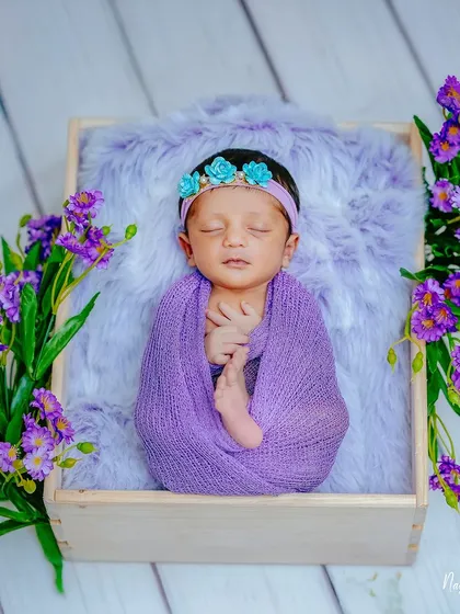 A top-down view of the purple floral setup, showcasing the beautiful symmetry of the arrangement. The baby is the peaceful center of this vibrant and artfully composed newborn photograph.