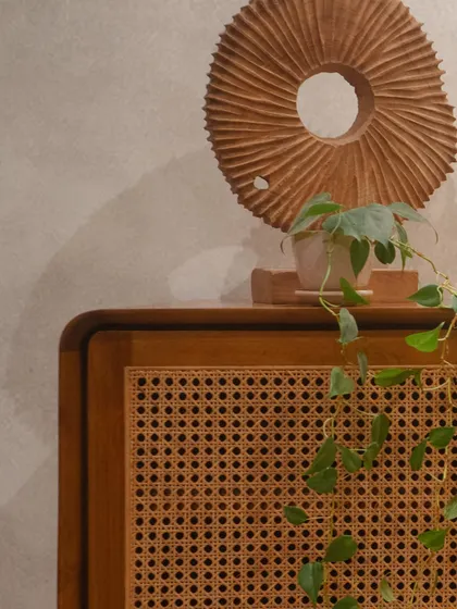A detail of the 'Kayo' cabinet, showing the beautiful texture of the rattan door, complemented by a decorative wooden piece and a trailing plant.