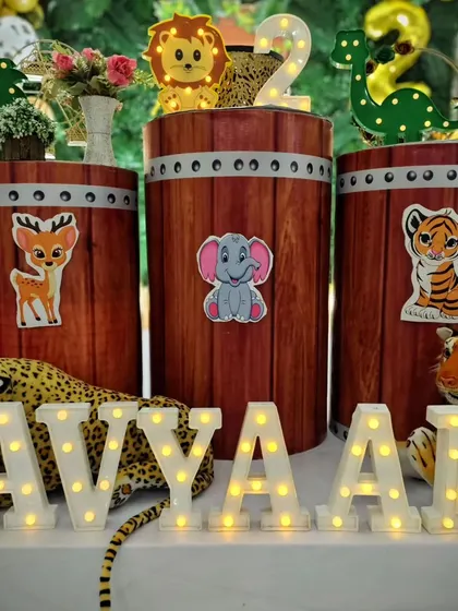 The cake table setup for Avyaan's party, with barrel-style plinths decorated with cute animal sticker's and the child's name in marquee letter's.