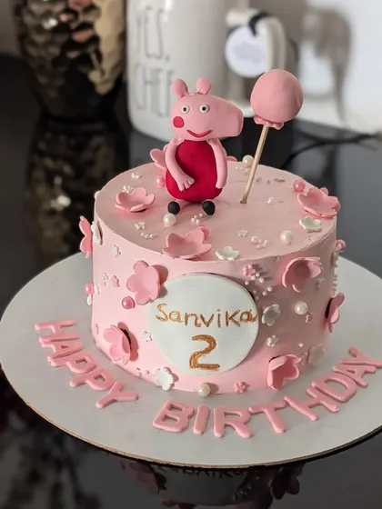 A sweet Peppa Pig cake for a second birthday. This pink cake features a handmade fondant Peppa figure holding a balloon, surrounded by little flowers.