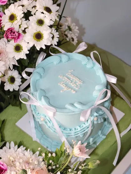 A close-up of the mini cake from our Women's Day hamper. The delicate white ribbons and piped details make it an incredibly elegant treat.