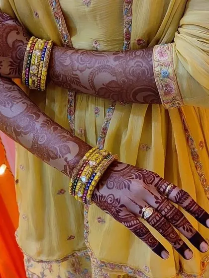 A beautiful shot of a client's mature henna stain. The deep color of the mehndi looks stunning against her yellow outfit and colorful bangles.