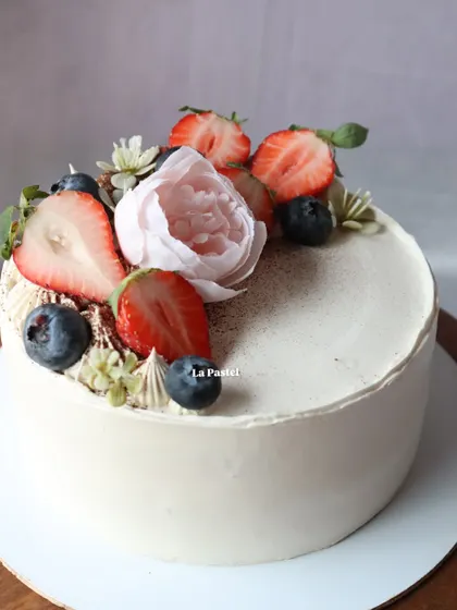 A beautiful vanilla cake decorated with fresh berries and a delicate pink sugar peony.