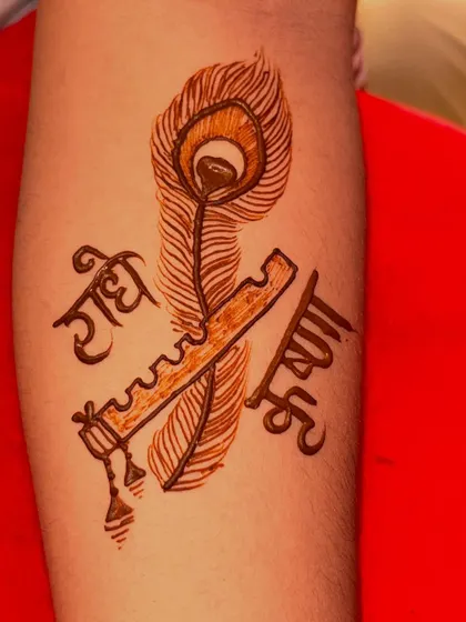 A simple and elegant design featuring 'Radhe Krishna' in Hindi script, intertwined with a flute and a peacock feather. This is a beautiful choice for festivals or for anyone wanting a touch of divine love.
