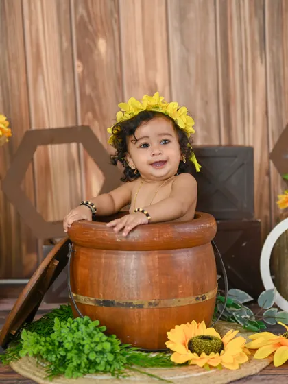 A sunflower-themed first birthday shoot. This little one is peeking out of a barrel, full of curiosity.