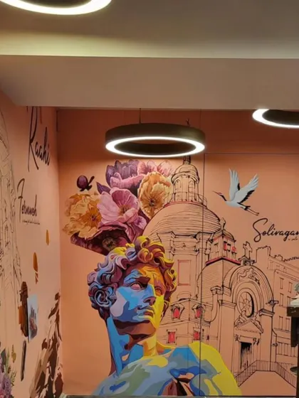 A colorful and eclectic mural for the travel-themed space 'Raahi'. This section features a vibrant portrait of a classical statue, overlaid with flowers and set against an architectural sketch, representing a journey through art and history.