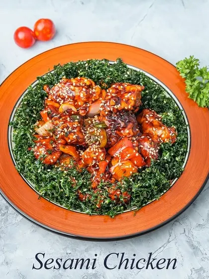 This dish features crispy chicken tossed in a dark, savory sauce and served on a bed of crunchy fried spinach, then garnished with toasted sesame seeds for added flavor and texture.