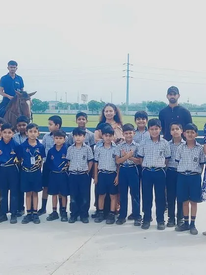 A class of students from Uma Public School poses for a group photo during their horse riding session, with instructors on horseback in the background.