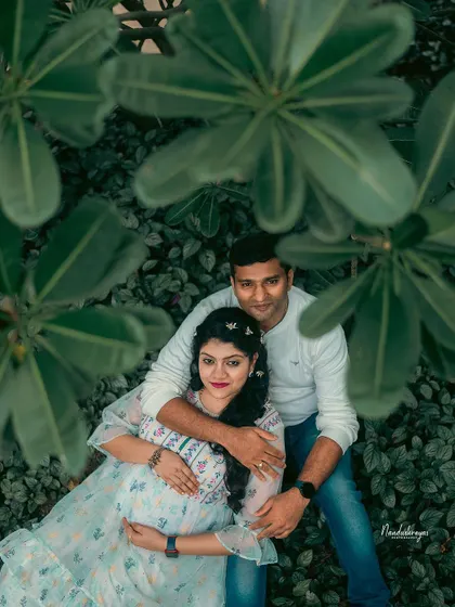 A high-angle shot of an expecting couple nestled among large green leaves. This creative perspective makes for a unique and intimate outdoor portrait.
