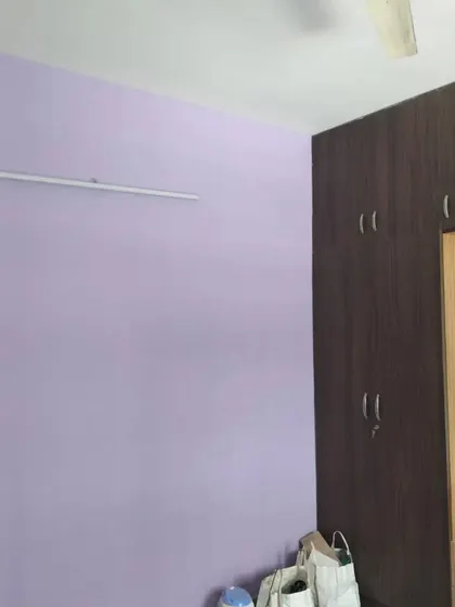 A bedroom featuring a freshly painted light purple wall next to a dark wood wardrobe, creating a pleasant contrast.