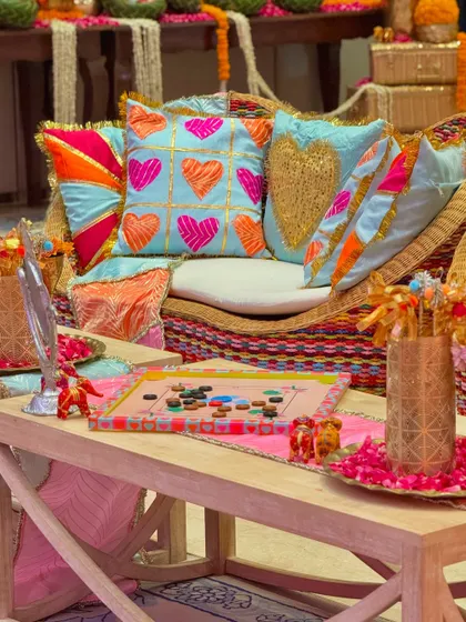 A detailed shot of the custom-designed cushions and playful elements from a Garba event. A hand-painted carrom board sits on the table, reflecting the nostalgic and fun theme of the celebration.