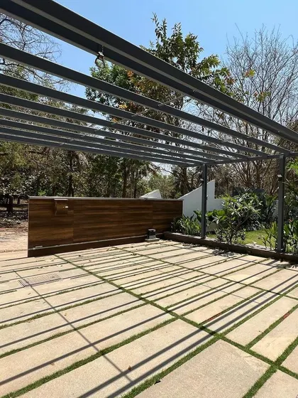The strong afternoon sun casts sharp, linear shadows from a large pergola over a driveway, turning a functional space into a graphic pattern.