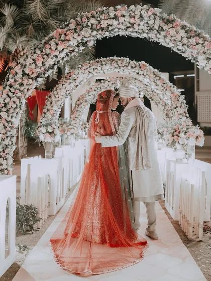 A tender moment between the couple under a floral archway, their silhouettes framed by the soft light. This image speaks of intimacy and shared promises.