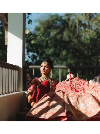 The bride sits in the soft morning light, her red lehenga laid out beside her. A quiet, beautiful moment of anticipation before the day's festivities begin.