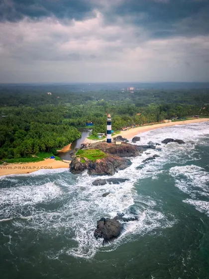 An aerial view of the Kaup lighthouse standing strong against the powerful waves of the monsoon season. This perspective shows the dramatic meeting of land and sea on the Karnataka coast.