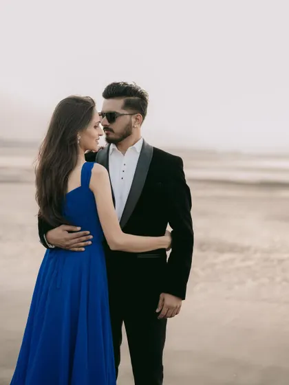 A classic, romantic pose on the beach. The groom's sharp tuxedo and the bride's elegant blue gown create a perfectly coordinated look for their pre-wedding photos.