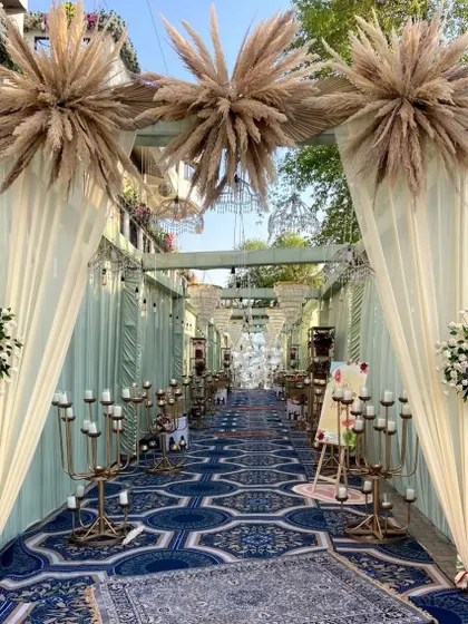 An elegant blue and white themed entranceway. The decor features a printed carpet, candelabras, and drapes topped with pampas grass for a touch of boho chic.