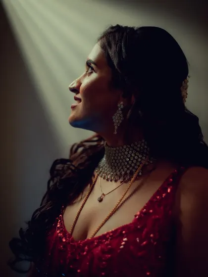 A hopeful and cinematic portrait of a bride looking up into a beam of light. The dramatic lighting highlights her profile and the sparkle of her red gown, creating a moment of magic.