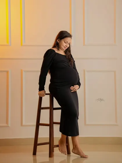 A classic maternity pose in a simple black dress. The warm side lighting beautifully defines the baby bump against the elegant white wall paneling.
